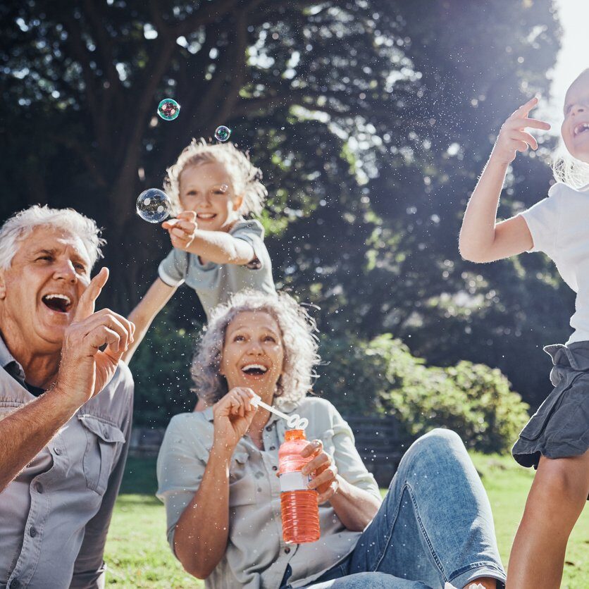 Grandparents, bubbles and children play in park happy together for fun, joy and outdoor happiness. Retired, smile and excited elderly senior couple, girl grandkids and love playing outside in nature